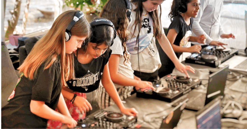 קבוצת ילדות עם אוזניות מתנסות בעמדות DJ מקצועיות בהפעלת יום הולדת של Follow the Beat.