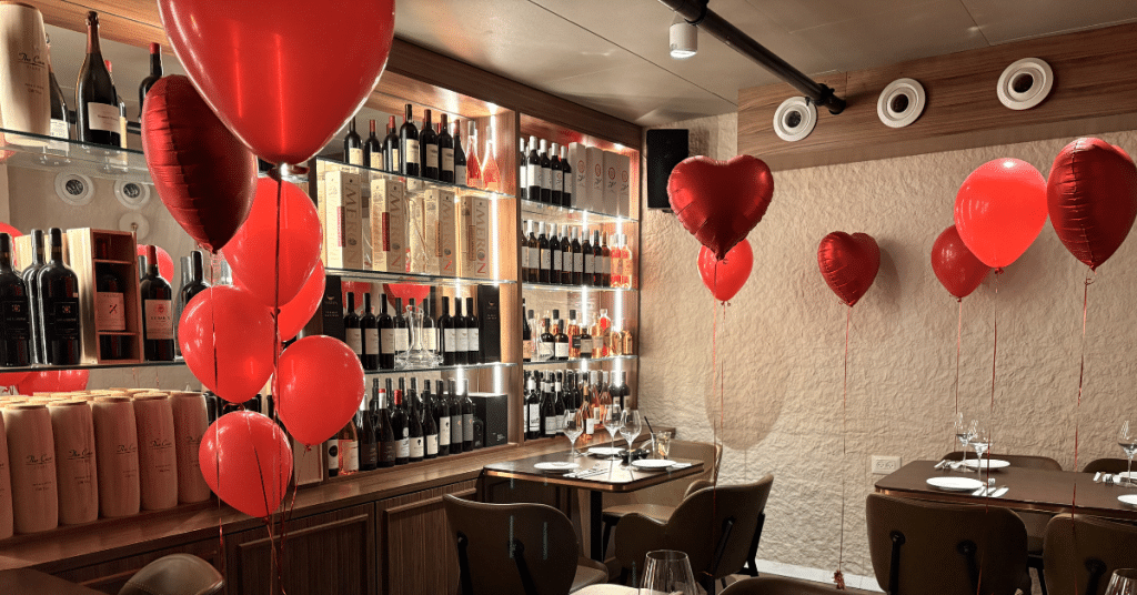 חלל אירועים בוטיקי ומעוצב בקומה מינוס אחד של גפן דלי (Gefen Deli) עם בלוני לב אדומים ומדפי יין עשירים.