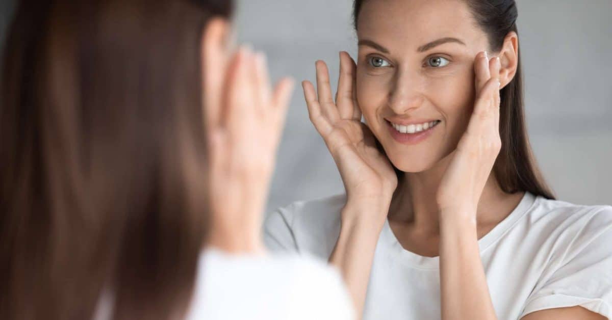 Attractive,Smiling,Young,Brunette,Woman,Looking,At,Mirror,,Touching,Face.