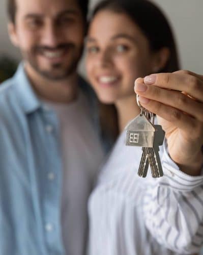 Crop close up of excited young Caucasian couple show keys to new shared home or dwelling. Happy man and woman spouses feel overjoyed moving relocating to own house. Rental, real estate concept.